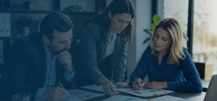 Three financial experts reviewing earnings reports, cash flow charts, and business records during a Quality of Earnings analysis.
