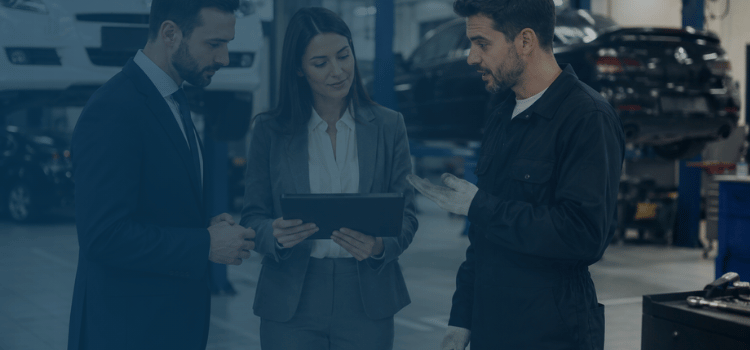 Business consultants and an automotive technician reviewing franchise operations inside a professional auto repair shop.