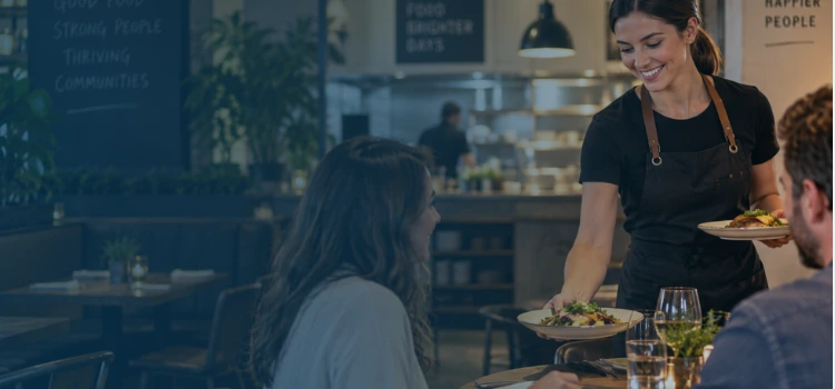 Woman server delivering meals to customers in a modern restaurant, illustrating restaurant operations and prime cost management.
