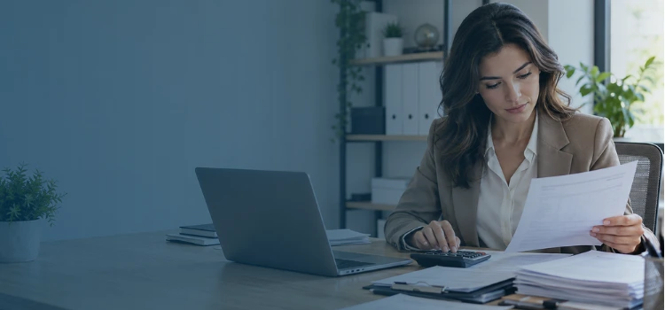 Businesswoman reviewing invoices and using a calculator to analyze the accounts payable turnover ratio and manage vendor payments.